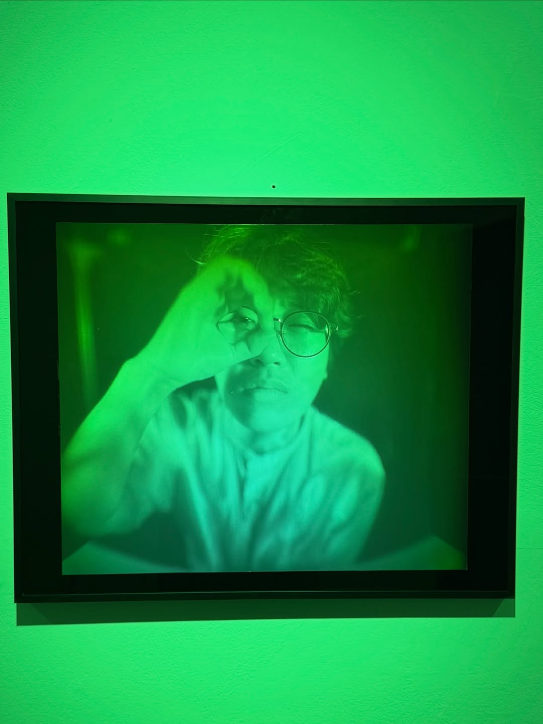 Framed green hologram self-portrait, hand raised over the artist's face