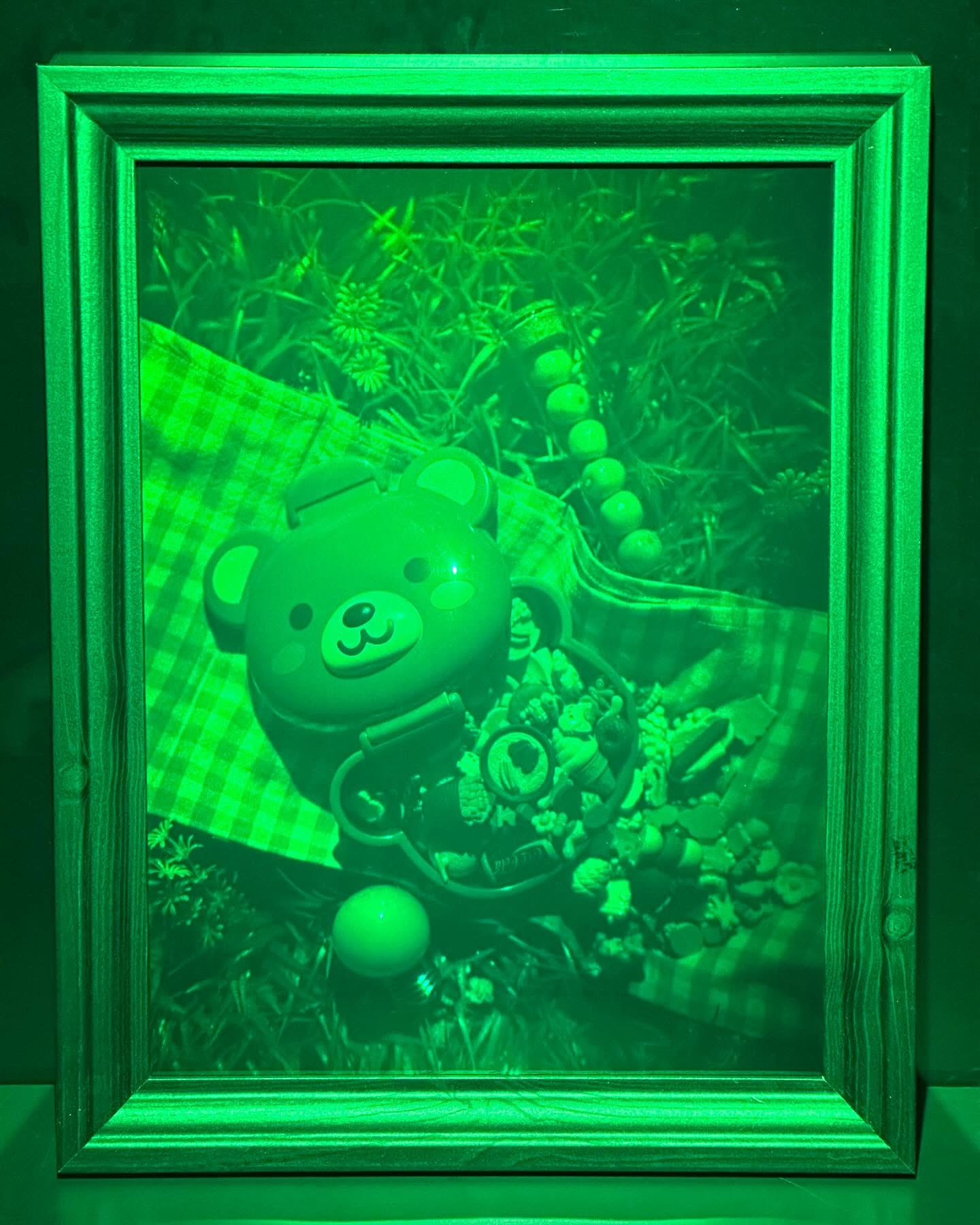 Green framed hologram of a bear-shaped lunch box on gingham cloth with toys