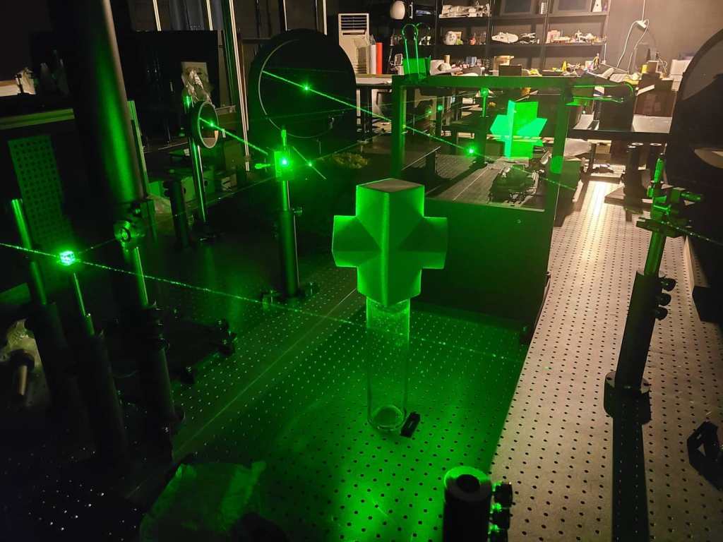 Laser beams crossing an optical table with mirrors and mounts in the dark studio